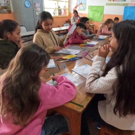 Grupo de niños sentados alrededor de una mesa se entretiene dibujando con lápices de colores.
